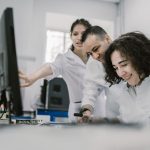 Equipe diversa de cientistas trabalha em conjunto diante de um computador em um laboratório moderno.