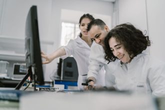 Equipe diversa de cientistas trabalha em conjunto diante de um computador em um laboratório moderno.