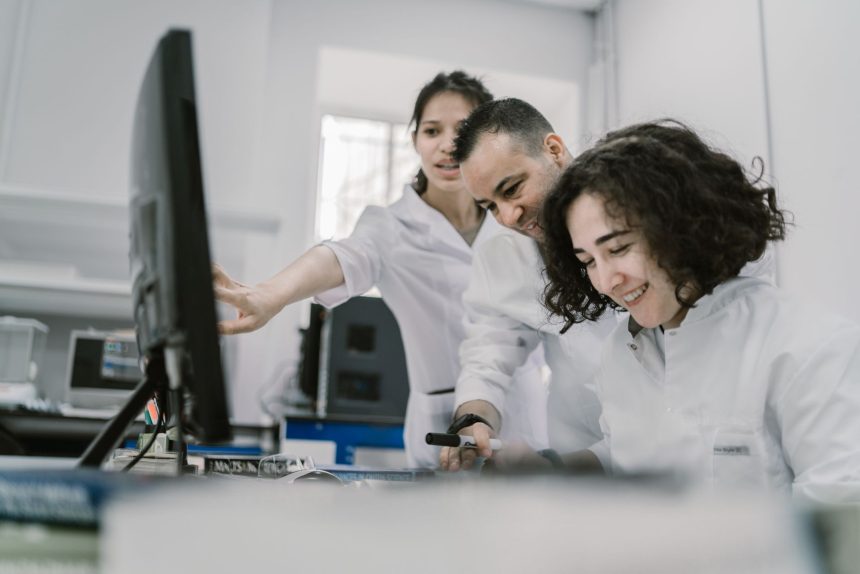 Equipe diversa de cientistas trabalha em conjunto diante de um computador em um laboratório moderno.