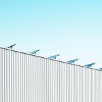 Edifício industrial com painéis solares no telhado sob céu azul.