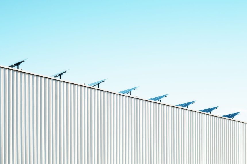 Edifício industrial com painéis solares no telhado sob céu azul.