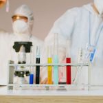 Dois cientistas usando equipamentos de proteção trabalham com tubos de ensaio em um laboratório moderno.
