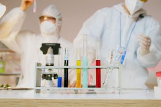 Dois cientistas usando equipamentos de proteção trabalham com tubos de ensaio em um laboratório moderno.