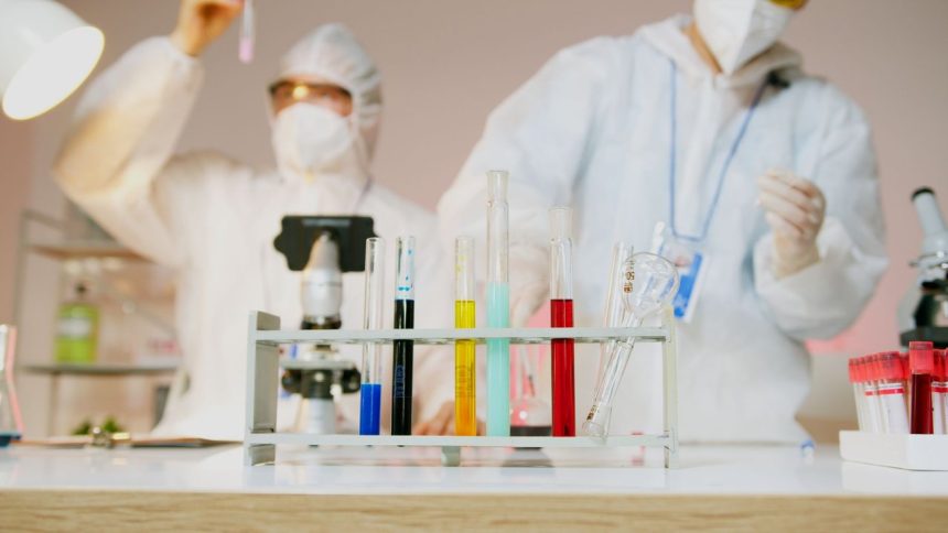 Dois cientistas usando equipamentos de proteção trabalham com tubos de ensaio em um laboratório moderno.