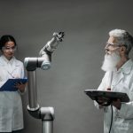 Dois pesquisadores analisam um braço robótico em um laboratório de tecnologia.