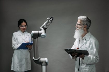 Dois pesquisadores analisam um braço robótico em um laboratório de tecnologia.